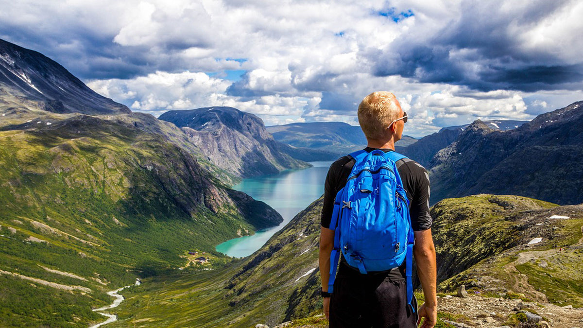 Man wearing a backpack looking out towards lakes and mountains