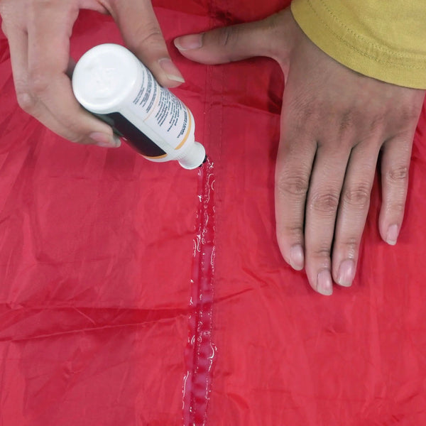 A person applying Gear Aid Seam Grip stitching waterproof sealant in a 60ml botttle with a brush head to a tent