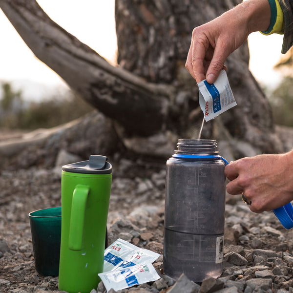 Lifestyle image of a person pouring in Care Plus electrolyte powder in to their water bottle 