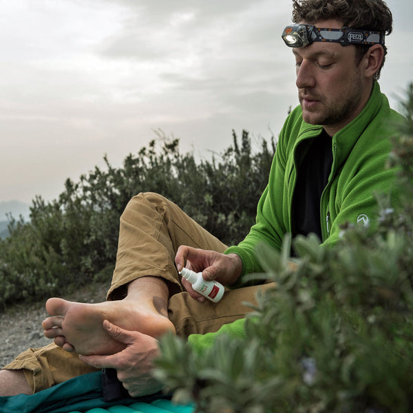 Lifestyle image of a man applying Care Plus blister prevention camphor spray to his feet whilst outdoors