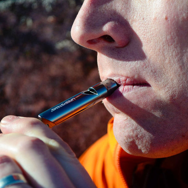 Lifesystems anodised aluminium mountain whistle in silver colour being blown outdoors by a mountaineer