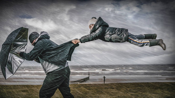 Man fighting against the wind with an umbrella whilst his child is holding his jacket as being picked up by the wind
