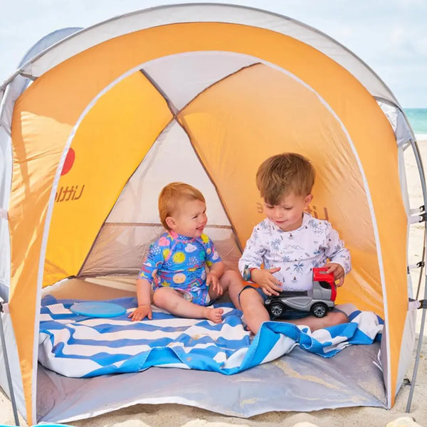 Lifetyle image of two toddlers playing inside a Littlelife compact beach shelter whilst at the seaside