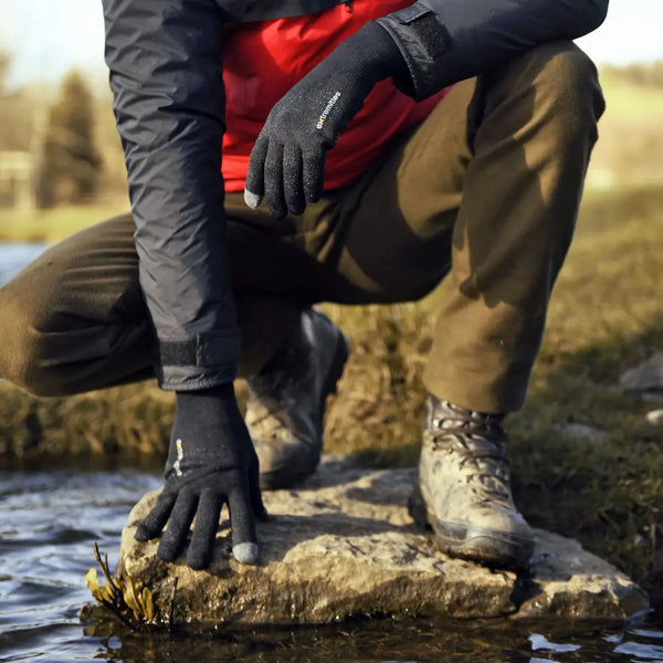 Lifestyle shot of a man wearing Extremities Evolution waterproof gloves crouched down by open water