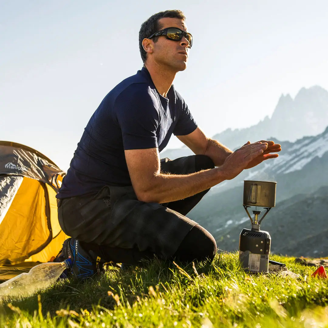 Lifestyle image of a man warming his hands over a gas stove  whilst wearing a Sub Zero Factor 1 Plus Mens short sleeve thermal base layer top in navy colour whilst mountaineering