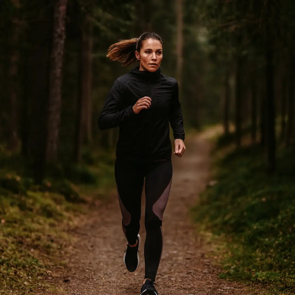 Woman running on a forest path wearing black athletic top and Sub Zero Factor 1 Plus stretch womens base layer leggings 