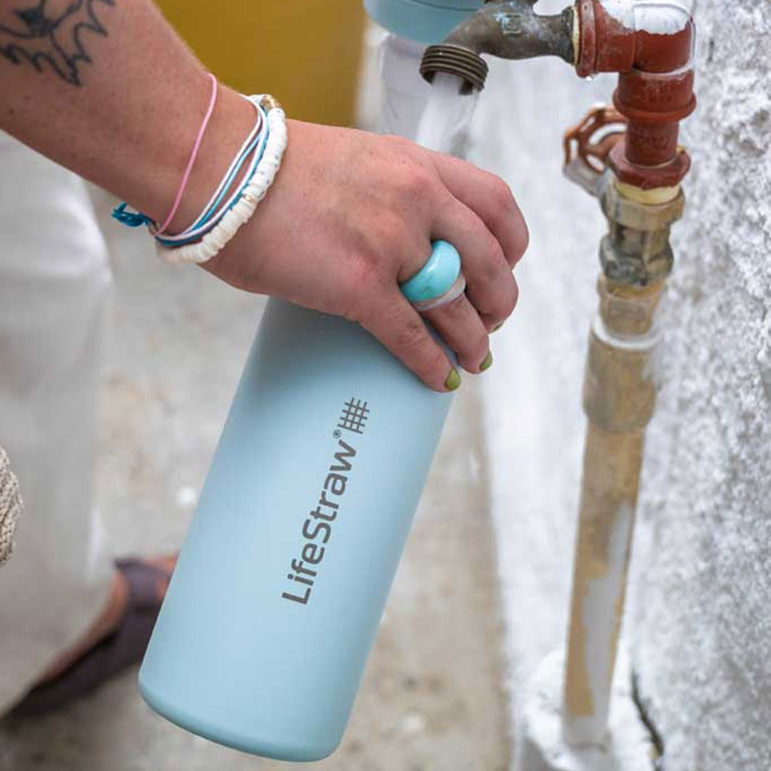 Lifestyle image of a woman filling up a LifeStraw vacuum insulated 530ml stainless steel Go Series water filter bottle from an outside tap