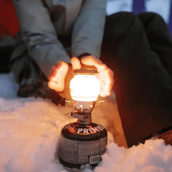 Person holding their hands to a lit Primus Easy Light gas lantern in the snow