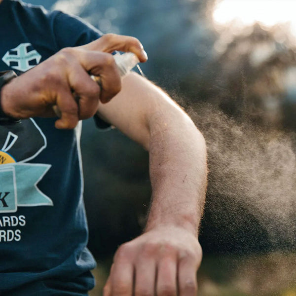 Lifestyle image of a man spraying Lifesystems expedition sensitive DEET free insect repellent on to his arm whilst outdoors