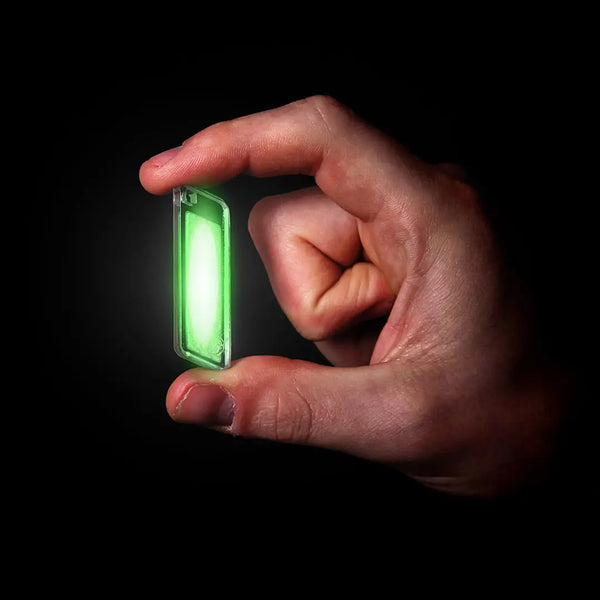 Lifesystems glow marker tag in green being held in someones hand in the dark 