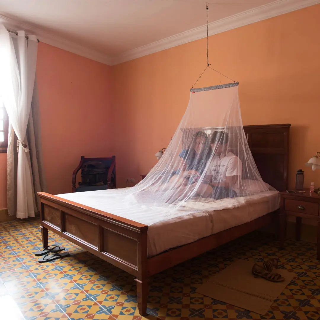 Two people in a hotel room lying on a double bed with a Lifesystems double micronet mosquito net protecting them