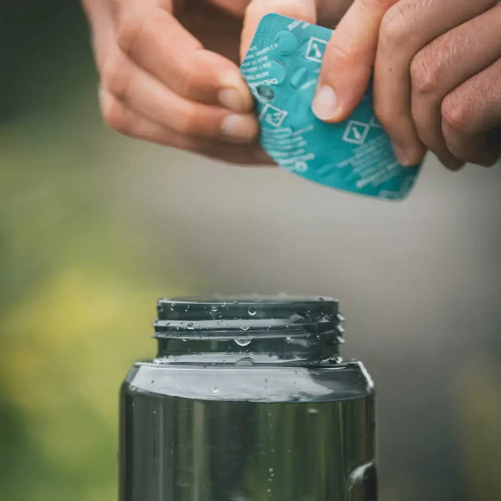 Person pushing out a Lifesystems Chlorine Dioxide Water Purification Tablet in to a bottle of collected water