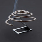 Lit single Lifesystems insect repellent coil on its burning stand on a grey background 
