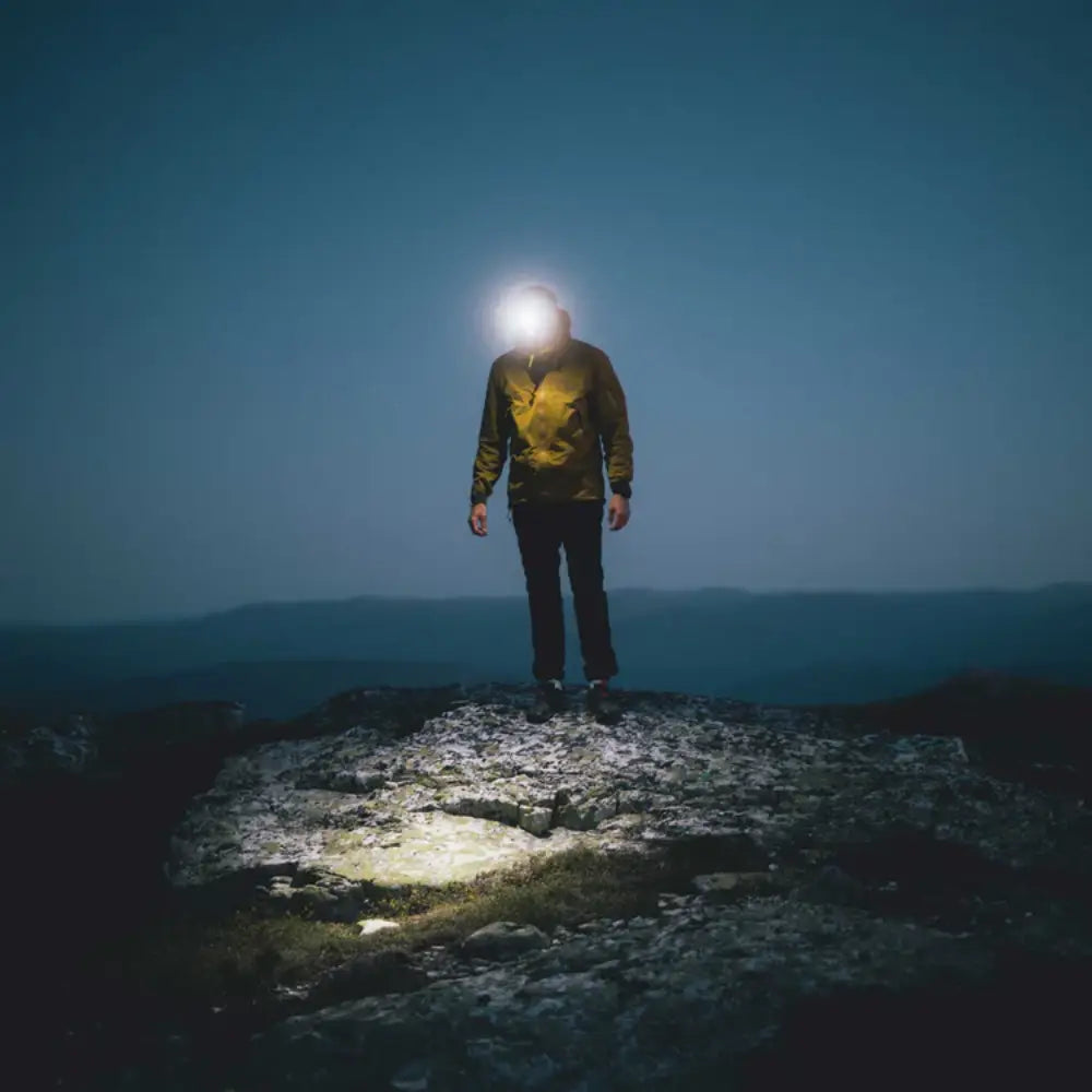 Person standing on a rocky outcrop at night with a Lifesystems 580 head torch illuminating the area.