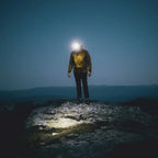 Person standing on a rocky outcrop at night with a Lifesystems 580 head torch illuminating the area.