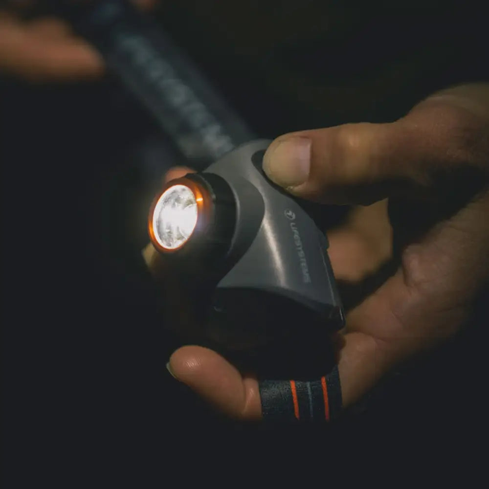 Hand holding a Lifesystems 580 head torch and switching it on with their thumb at night-time