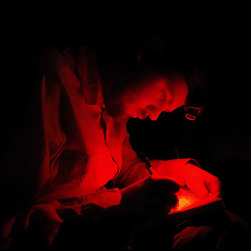 Man wearing a Lifesystems 580 head torch in red light mode whilst writing in a journal at night