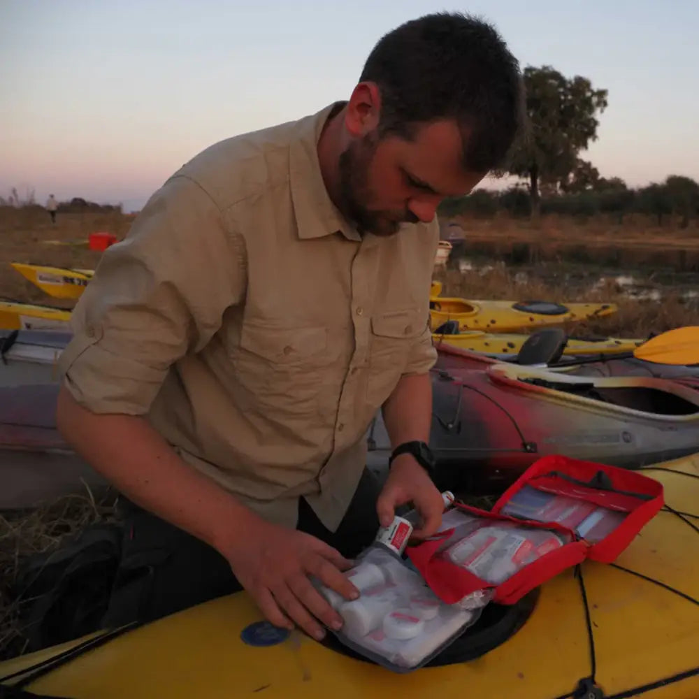 Man getting a bandgae out of a Lifesystems Mountain Leader Pro First Aid Kit whilst on a kayaking expedition