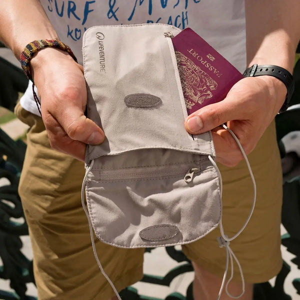 Lifetsyle image of a man holding a Lifeventure RFiD chest wallet in beiege in front of him showing a passport being held in the fornt zipped pouch and the zipped entry to the inner pouch