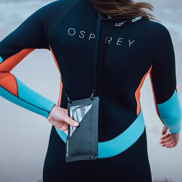 Woman in a wetsuit at the beach using a Lifeventure Waterproof Touchscreen Phone Pouch  to protect her mobile