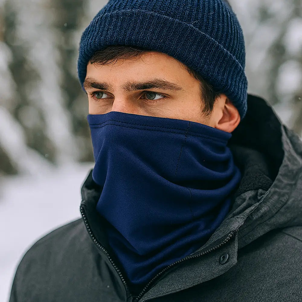 Man wearing a Sub Zero Meraklon Thermal Head Over In navy with a knitted hat outdoors in the snow. 