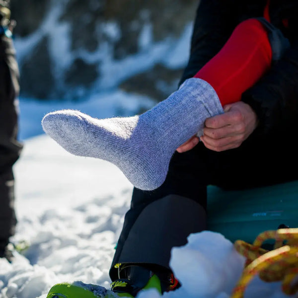 Lifestyle image of a person pulling Sub Zero merino wool walking socks in grey marl colour on to their feet whilst outside in the snow