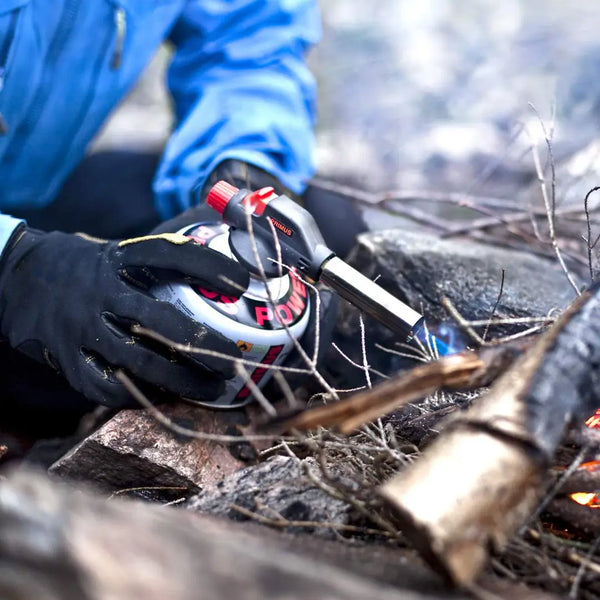 Person using a Primus Fire Starter on a camp fire with a blurred natural background