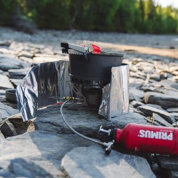 Primus heat reflector and windscreen installed around a backpacking stove on a beach
