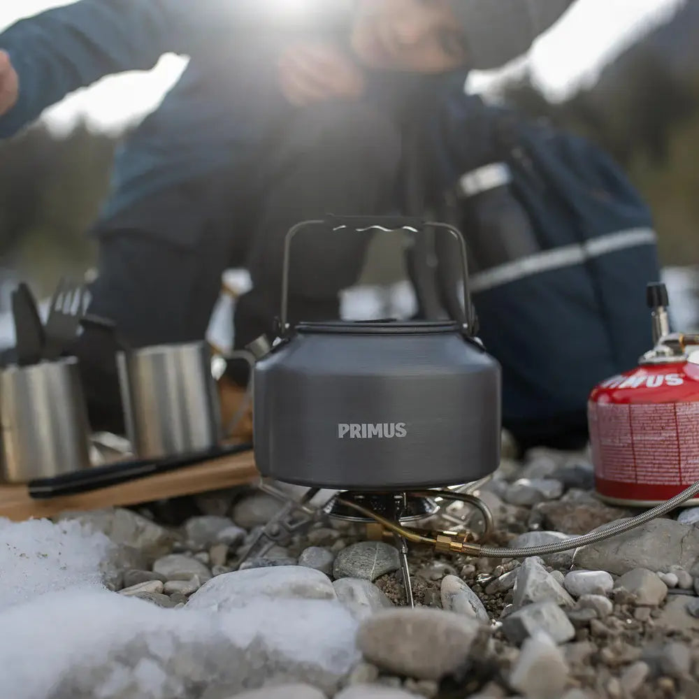 Primus Gravity camping stove with a Litech 1500ml kettle on top, nestled in rocky ground with a person in the background