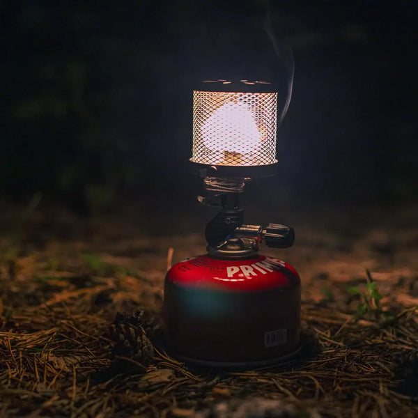 Camping lantern with visible brand Primus Micron Steel Mesh gas lantern lit on a dark background