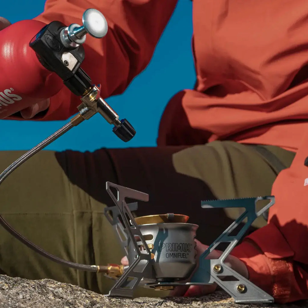 Lifestyle image of a person holding the fuel bottle whilst placing the Primus Omnifuel Expedition Multifuel Stove on the ground