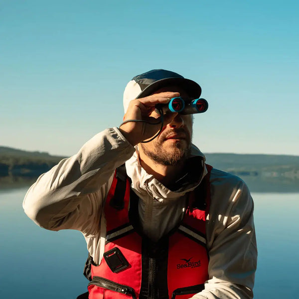 Lifestyle shot of a man sitting in a boat on a lake looking at something in the distance using his Silva pocket binoculars in 10X magnification