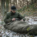 Lifestyle shot of a man using a Snugpak bivi bag in olive colour with his sleeping bag outdoors in winter