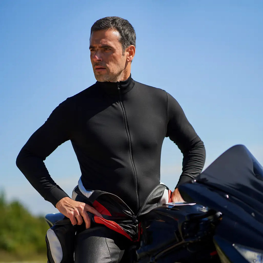 Man straddling his motorbike with his upper leathers peeled back to show the Sub Zero Factor 2 thermal mid layer onesie in black worn underneath