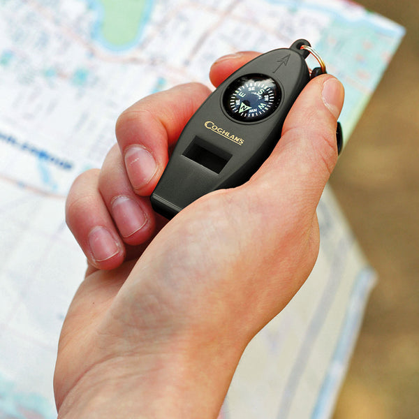 Coghlans four function whistle held in someones hand over a map